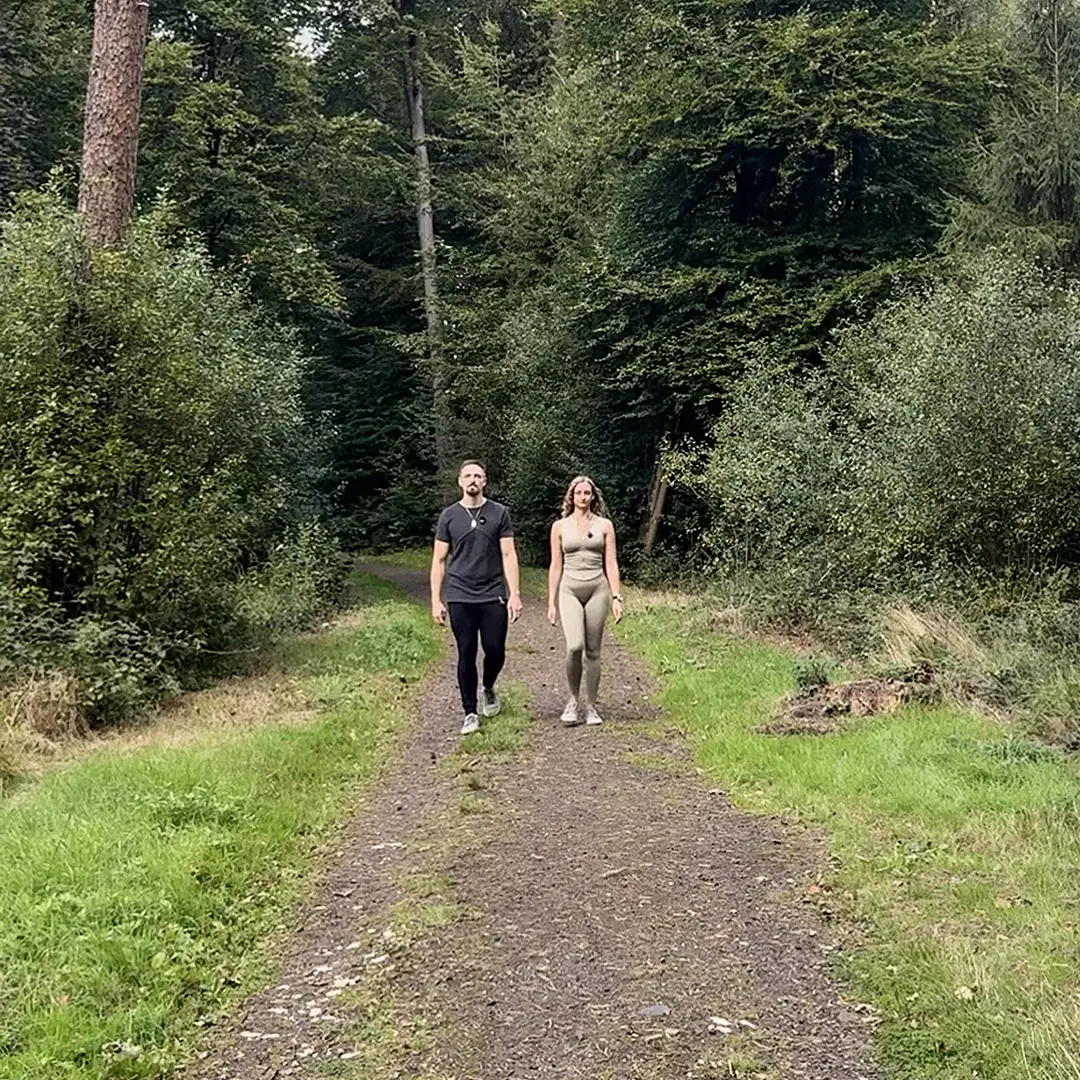 Outdoor-Training im Alltag: zwei Personen gehen auf einem Waldweg in der Natur.